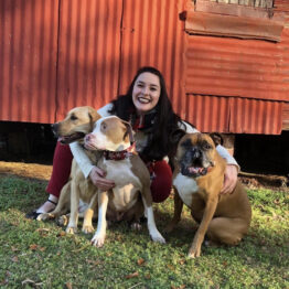 Rachel Kahn in the grass hugging three large dogs.