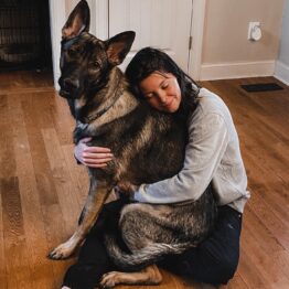 Britta Duffy hugging large dog as he sits in her lap.